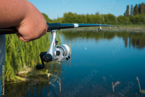 Fishing rod in hand on a background of lake.