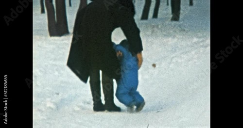 Funny little child falls on slippery snow in winter, mother helps to get up. Small kid in blue jacket walks with mother in snowy park. Happy family. Vintage color film. Family archive. Retro 1980s