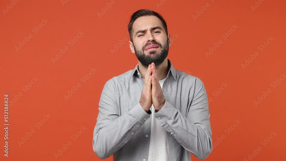 Pleading vivid young brunet man 20s years old wears blue shirt hold hands folded in prayer begging about something making wish keep fingers crossed isolated on plain orange background studio portrait Pleading vivid young brunet man 20s years old wears blue shirt hold hands folded in prayer begging about something making wish keep fingers crossed isolated on plain orange background studio portrait