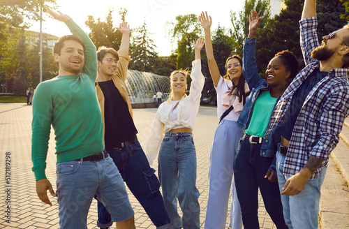 Group of happy young friends hanging out and having fun. Team of cheerful diverse people standing together on city square on sunny summer evening, stacking their hands and then raising them up in air