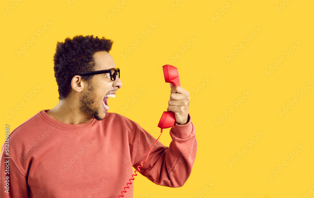 Side view man with angry face expression shouting at stupid call center tech support service line helpdesk operator. Scared shocked terrified or enraged guy on yellow color holding old phone receiver Side view man with angry face expression shouting at stupid call center tech support service line helpdesk operator. Scared shocked terrified or enraged guy on yellow color holding old phone receiver