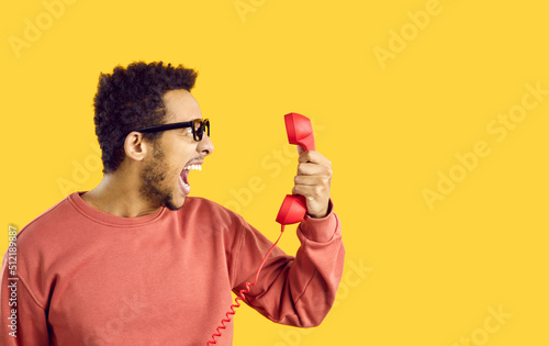 Side view man with angry face expression shouting at stupid call center tech support service line helpdesk operator. Scared shocked terrified or enraged guy on yellow color holding old phone receiver