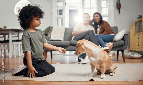 Its a treat for a trick. Shot of a little boy bonding with his dog while his parents sit in the background. © N Felix/peopleimages.com