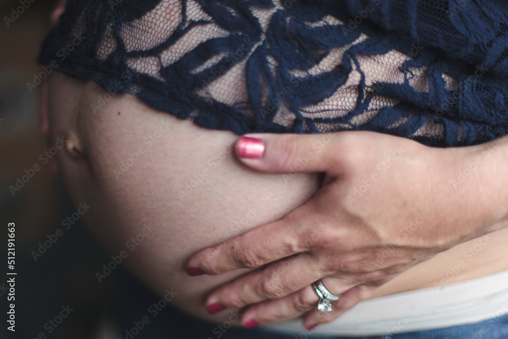 A woman holds her hands on her pregnant belly.