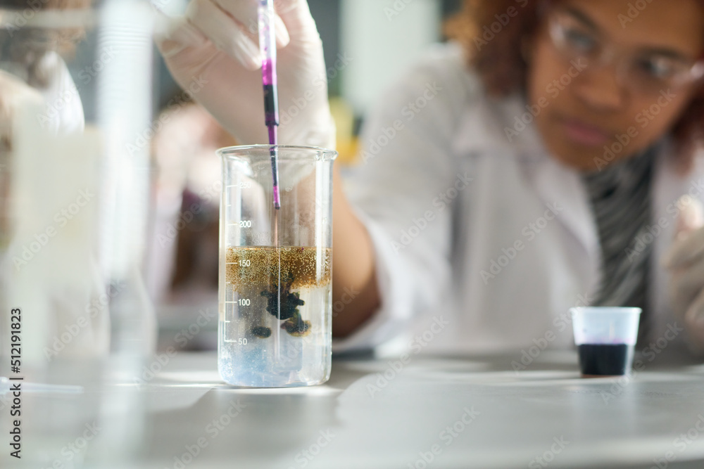 Female highschool student or researcher adding several drops of purple ink into glass containing transparent liquid chemical substance Female highschool student or researcher adding several drops of purple ink into glass containing transparent liquid chemical substance