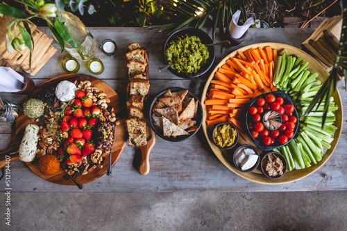 Vintage wood table with delicious and colorful vegetarian/vegan catering with celery, cherry tomatoes, carrot, hummus, avocado, toasts and olive, vegan gourmet cheese,  strawberries, nuts and crackers