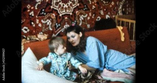Mother feeds baby with spoon in home room. Young, beautiful woman begs her child to eat in Soviet apartment interior. Happy parents care about child. Vintage color film. Family archive. Retro 1980s