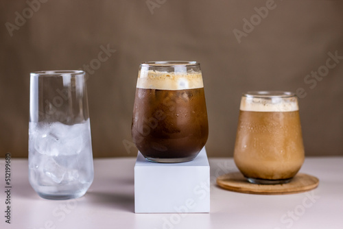 Cold coffee summer drink concept. Different size transparent glasses with ice cube and iced coffee on pastel brown background.