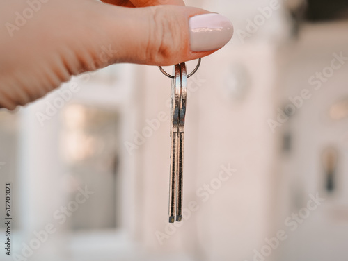 Woman's hand with metal keys on blurred background with house. High quality photo