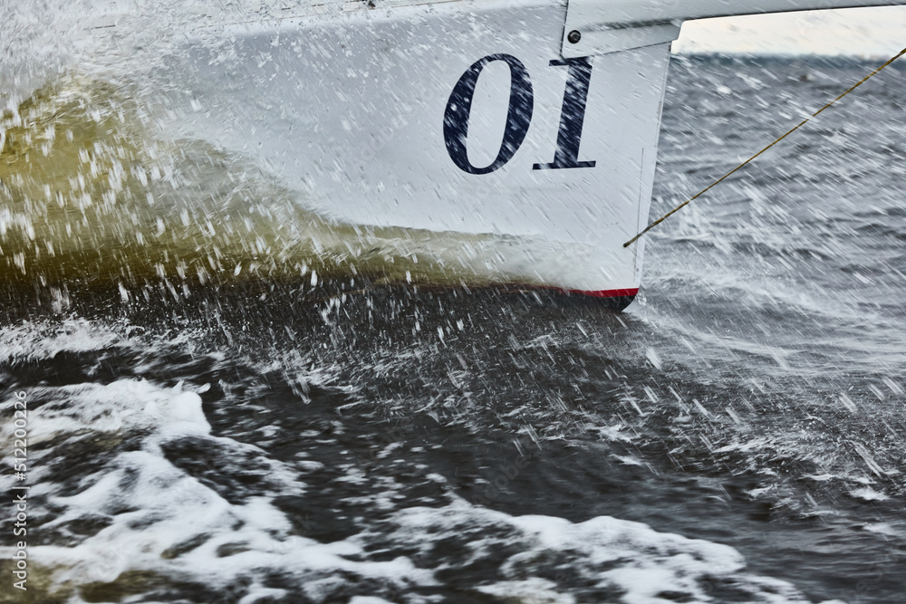 Naklejka premium the bow of the boat cuts through the water, bowsprit of sailing yacht in sailing regatta at stormy weather, splashes of water, hot racing, number one