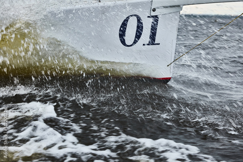 the bow of the boat cuts through the water, bowsprit of sailing yacht in sailing regatta at stormy weather, splashes of water, hot racing, number one