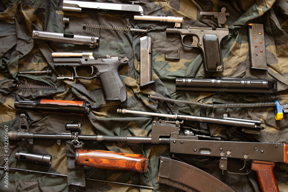 A disassembled machine gun and a pistol lie on a green camouflage background, military weapon, machine gun of a Ukrainian soldier A disassembled machine gun and a pistol lie on a green camouflage background, military weapon, machine gun of a Ukrainian soldier