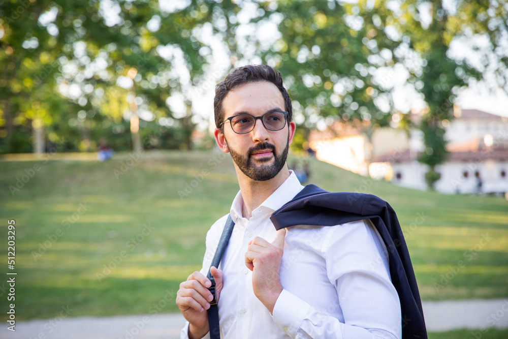 Young businessman with dark jacket over his shoulders and white shirt in a public garden Young businessman with dark jacket over his shoulders and white shirt in a public garden