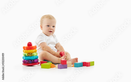 Cute baby plays with toys on a white isolated background. The child folds a constructor and a pyramid