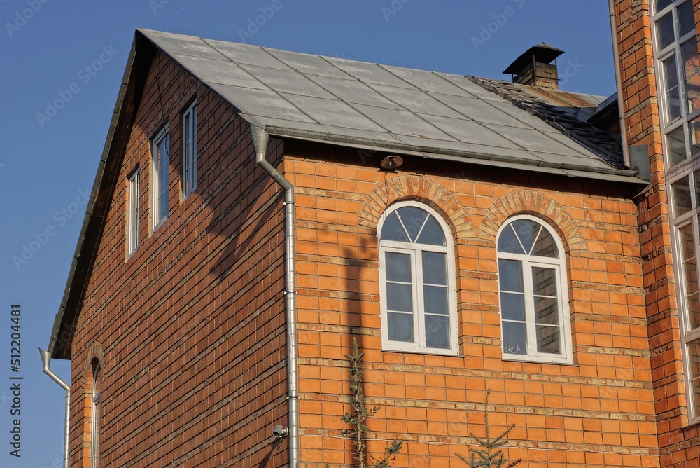 attic of a private red brick house with white windows under a gray slate roof outdoors against a blue sky