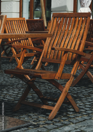 There are no people on the wooden terrace  on which there are wooden chairs  on the dark wooden floor. A deserted street cafe with wooden chairs. Street cafe  bistro  restaurant.