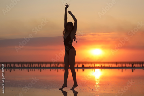 silhouette of a young slim woman in a swimsuit who dancing at sunset on the sea. summer holiday © Andriy Medvediuk