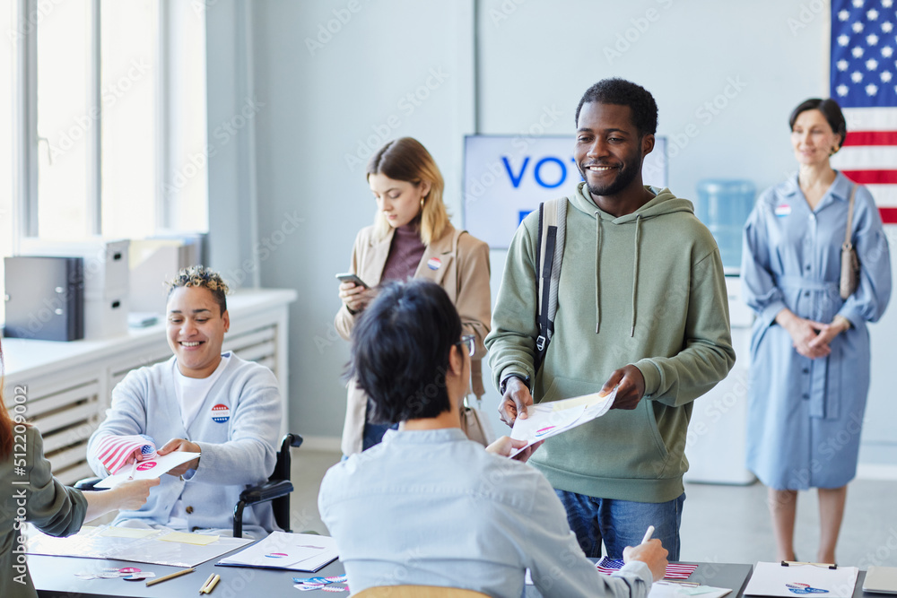 © Seventyfour - Diverse group of people voting in line and receiving ballot forms focus on smiling black man, copy space