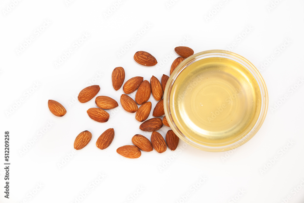Sweet almond oil in glass bowl, first extraction, and dry almond nuts as ingredient for confectionery close up on white backgrounds