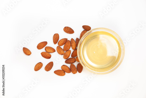 Sweet almond oil in glass bowl, first extraction, and dry almond nuts as ingredient for confectionery close up on white backgrounds