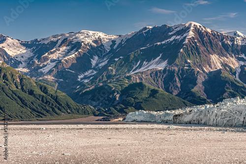 Disenchantment Bay, Alaska, USA - July 21, 2011: Floating ice field and Hubbard Glacier ice wall at ocean level. Snow covered mountain range on horizon under blue cloudscape. Forested slopes photo