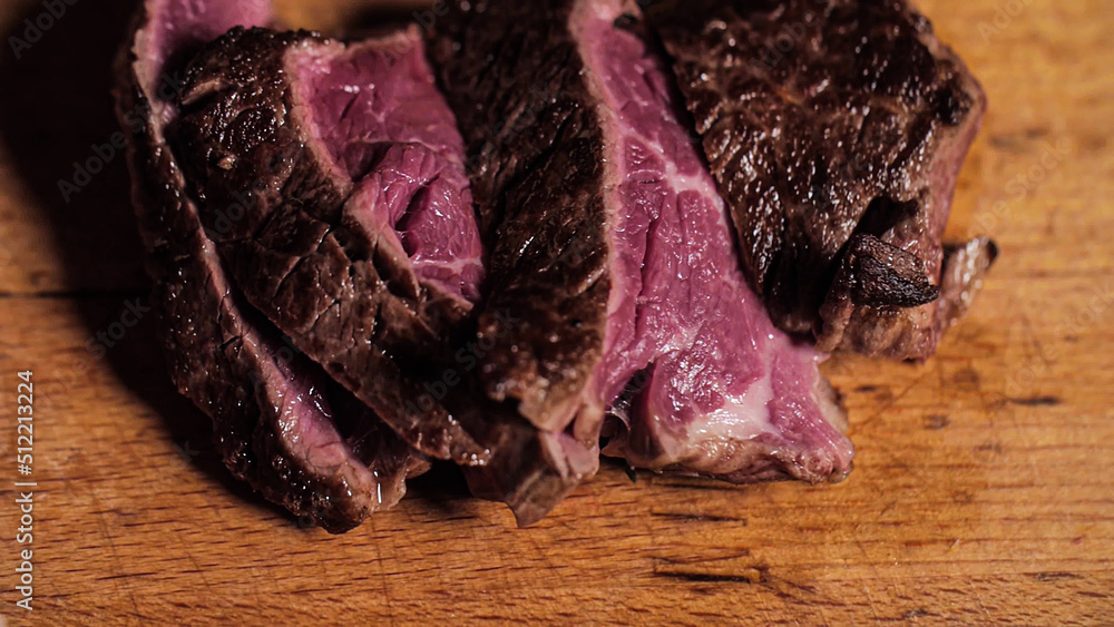 Obraz premium Adding a salt on a roasted juicy rare steak on a wooden cutting board. Close-up