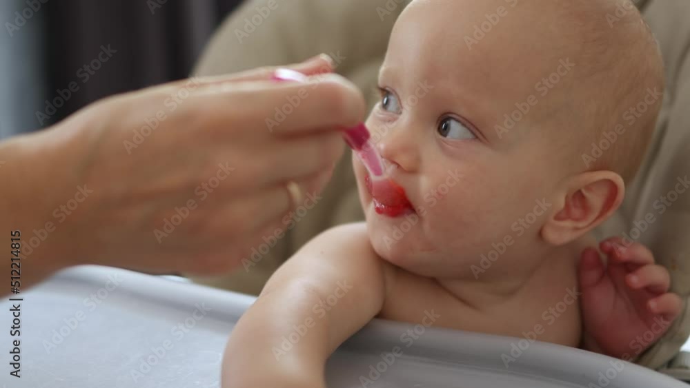 closeup portrait baby eating soup with spoon, making funny face, tasting food first time. caucasian baby child toddler kid feeding with spoon, sitting in feeding high chair. mash puree vegetables closeup portrait baby eating soup with spoon, making funny face, tasting food first time. caucasian baby child toddler kid feeding with spoon, sitting in feeding high chair. mash puree vegetables