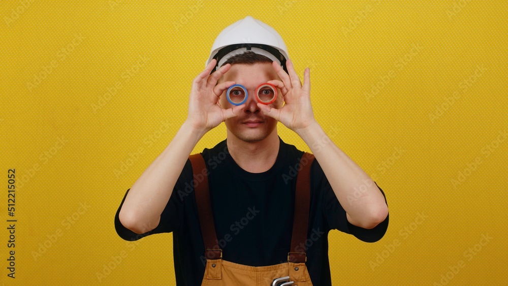 Funny smiling electrician in hardhat holds insulating tape in his hands. Electrician posing on yellow background Funny smiling electrician in hardhat holds insulating tape in his hands. Electrician posing on yellow background
