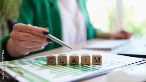 Woman pointing with pen on word claim made with wooden cubes in row photo