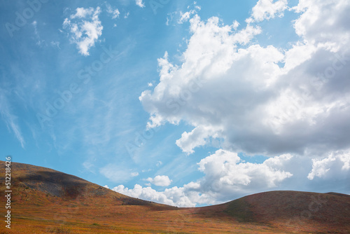 Motley autumn mountain landscape with sunlit hill tops under cloudy sky. Vivid autumn colors in mountains. Cirrus clouds above multicolor hills. Sunlight and shadows of clouds in changeable weather.