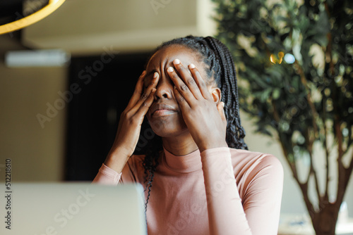 Картината върху платно Young unhappy afro american woman with dreadlocks crying covering eyes with hands in coffee house closeup