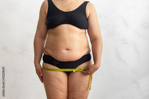 Cropped naked overweight woman body in bikini doing roulette tape measure of hips, leg volume, buttocks. Unhealthy, obesity lifestyle. Break down of subcutaneous, visceral fat. White background