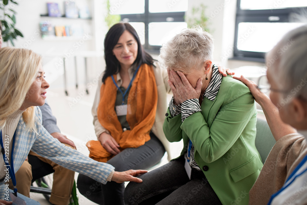 Group of senior people sitting in circle during therapy session, consoling depressed woman.