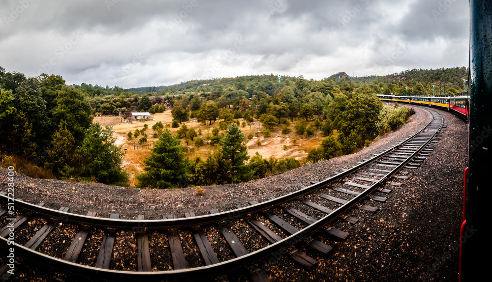 Obraz premium railway and green train at cloudy day with nature landscape in the background, chepe train in chichuahua 