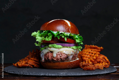 Gourmet burger on pretzel roll surrounded by sweet potato waffle fries on slate plate