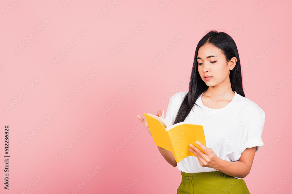 Portrait of beautiful Asian young woman teenage smiling holding a yellow book and reading, studio shot isolated on pink background with copy space Portrait of beautiful Asian young woman teenage smiling holding a yellow book and reading, studio shot isolated on pink background with copy space