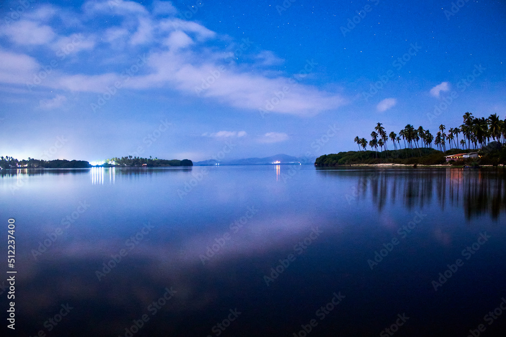 beautiful lake at night with blue and dark sky, palm trees in the background and reflections in the water, coyuca lagoon in pie de la cuesta, acapulco guerrero 