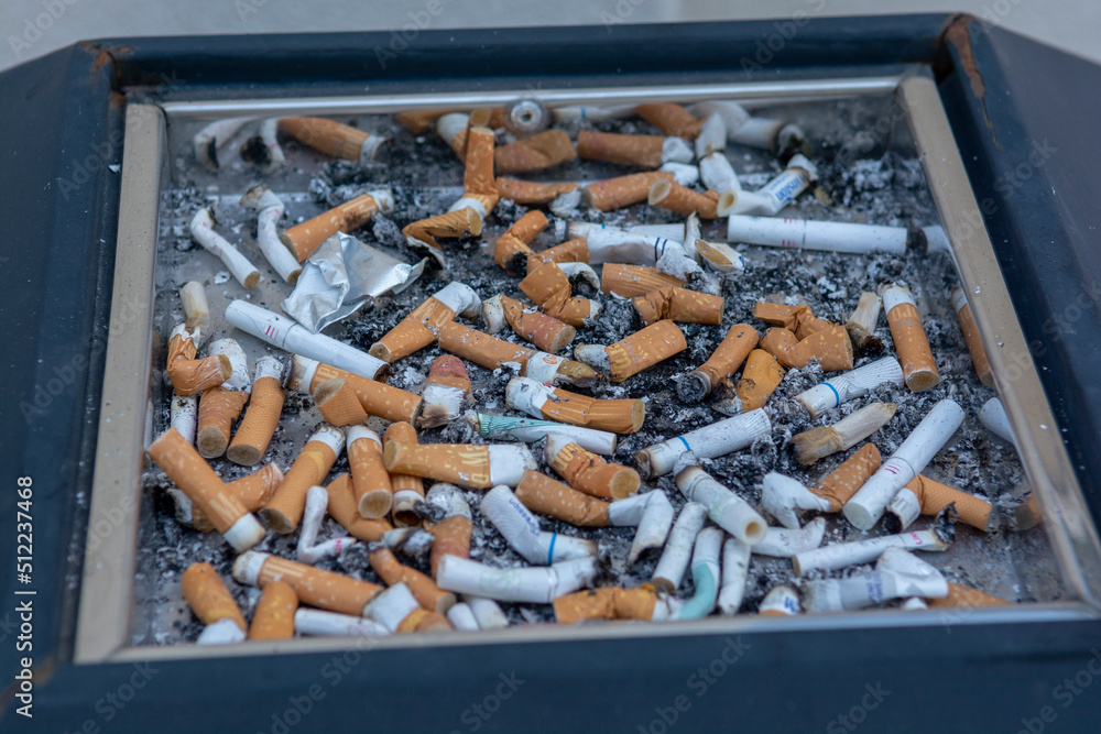 Many of cigarette butts in a big public ash tray. Stacked cigarette butts. Many of cigarette butts in a big public ash tray. Stacked cigarette butts.