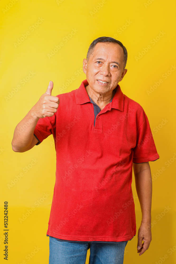 Asian senior man wearing casual t-shirt standing over isolated yellow background doing like thumbs up gesture with hand. Approving expression looking at the camera showing success. Asian senior man wearing casual t-shirt standing over isolated yellow background doing like thumbs up gesture with hand. Approving expression looking at the camera showing success.