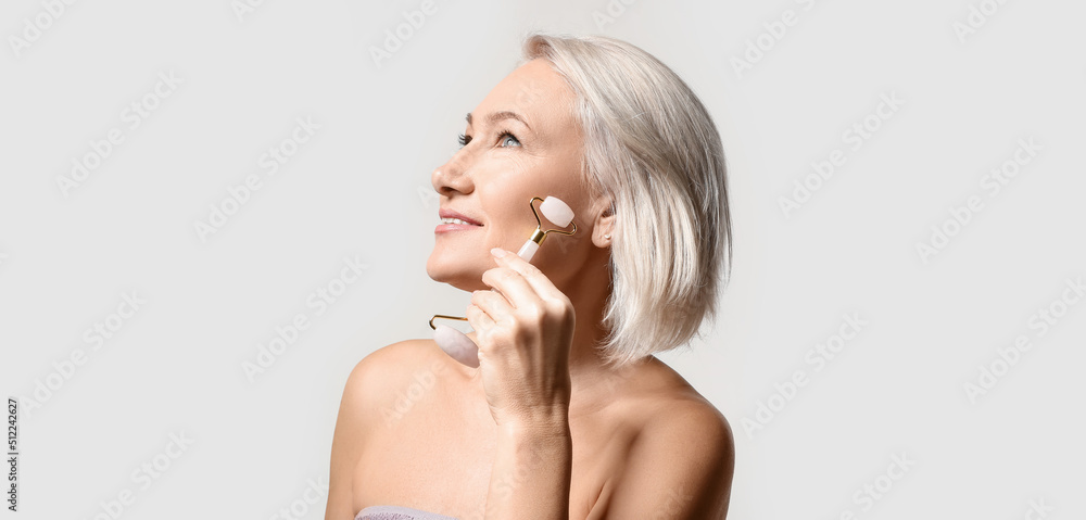 Mature woman with facial massage tool on light background Mature woman with facial massage tool on light background