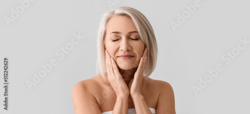 Mature woman giving herself face massage on light background photo