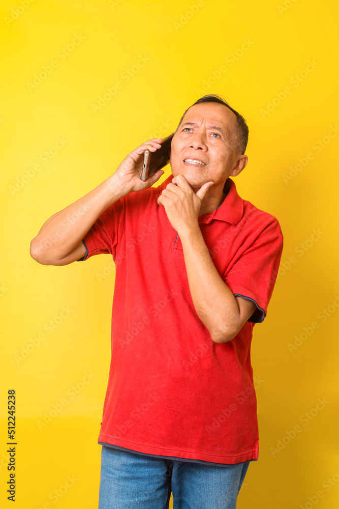 Senior man talking to telephone and thingking, wear red t shirt isolated on yellow background. Senior man talking to telephone and thingking, wear red t shirt isolated on yellow background.