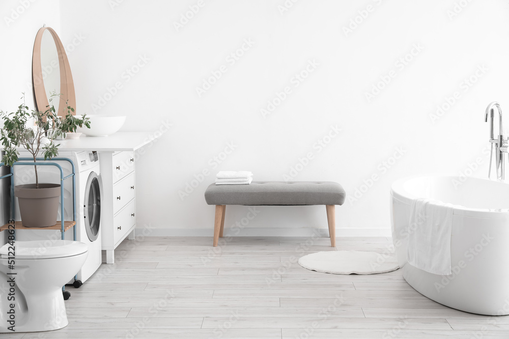 Interior of light bathroom with soft bench and washing machine