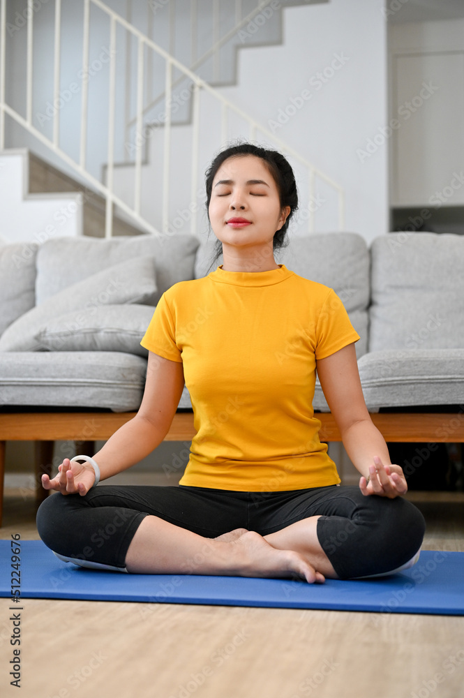Relaxed calm young Asian woman practicing yoga at home, meditating