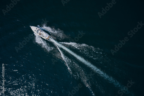 Modern big white boat with people moving fast on dark water top view. White yachts in the sea.