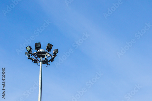 Spotlight on a high mast in the sky with clouds and protective mesh