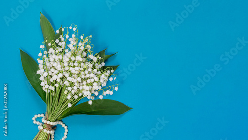 layout with a bouquet of lilies of the valley on a blue background, a delicate greeting card with a copy of the space