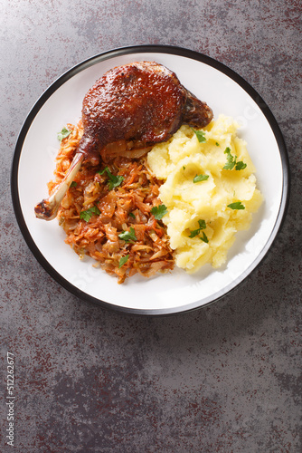 Romanian Rata pe varza duck leg serving with mashed potatoes and stewed cabbage close-up in a plate on the table. Vertical top view from above photo