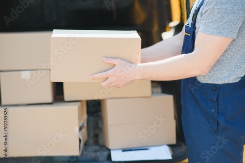delivery service employee. Portrait of man working in delivery service. Portrait of courier with box. Courier next to minivan. Delivery service career. © Serhii