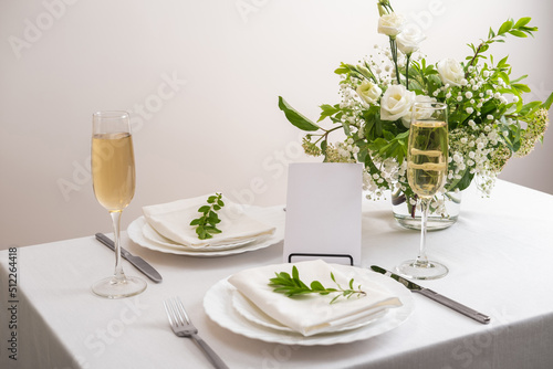 Mockup white blank space card for table number or menu. Wedding teble decoration with white flowers  glasses and white napkins. Elegantly decorated table at a wedding reception. 